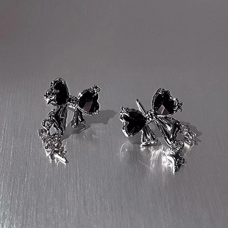 Black gemstone bow earrings with silver-tone accents on metallic background