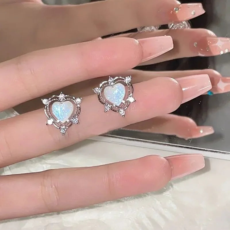 Heart-shaped opal stud earrings with crystal accents showcased on manicured hand