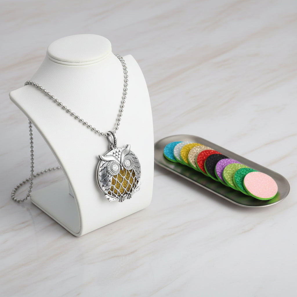 Silver owl-shaped locket with a chain and colorful round perfume pads on a white background.