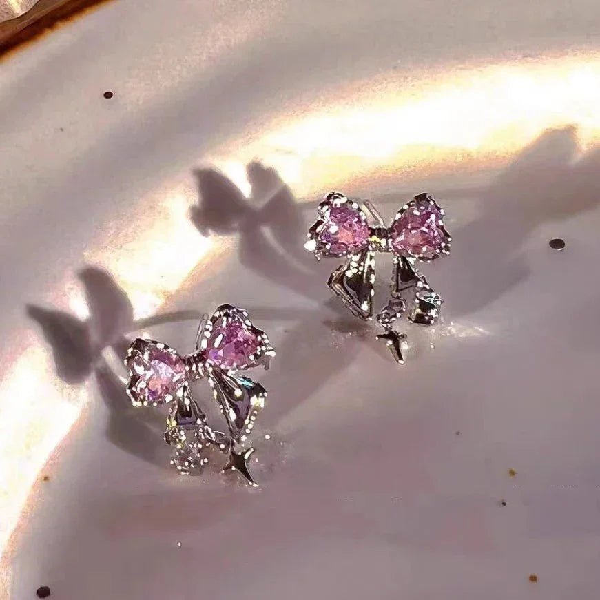 Pink crystal bow stud earrings with silver accents on a reflective surface