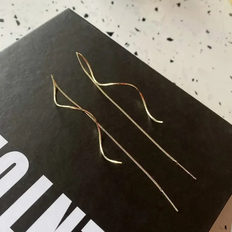 Pair of minimalist gold threader earrings with curved design on black background