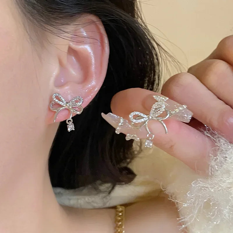 Silver bow-shaped earrings with crystal accents on woman's ear, matching decorative ring